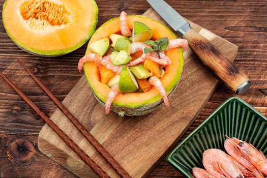 Delicious Asian salad of melon, shrimp and avocado in a half of melon on wooden table.
