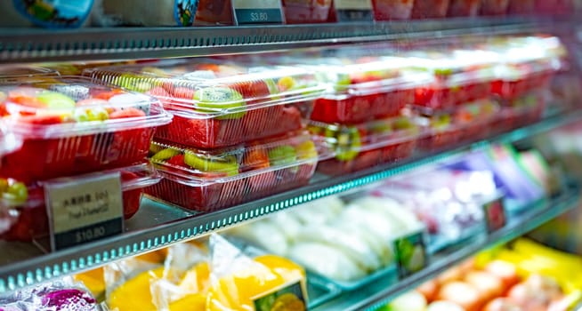 Plastic boxes with fresh fruits displayed in a commercial refrigerator. Fruit salad