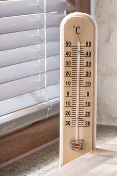 A wooden thermometer with an analog scale measuring the temperature placed near the window