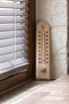 A wooden thermometer with an analog scale measuring the temperature placed near the window