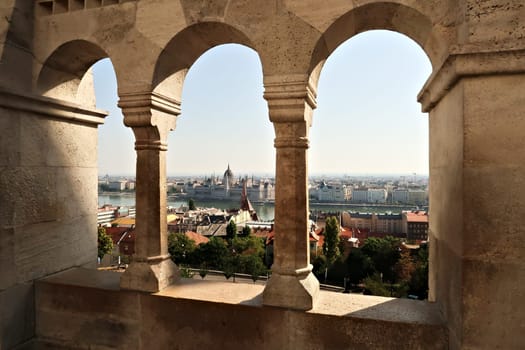View through a stone window of the Fisherman's Bastion onto the Hungarian Parliament Building at the Danube River, Budapest, Hungary 2022