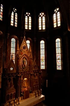 Elaborate altar in front of colorful stained glass windows in gothic style shape inside the Matthias Church, Budapest, Hungary 2022