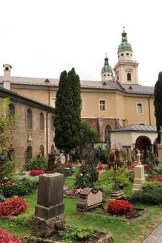Graves on the St., Saint Peter's Cemetery, Petersfriedhof in front of two bell towers, clock towers of the St. Peter's Abbey, Monastery, Stift Sankt Peter, Salzburg, Austria 2022