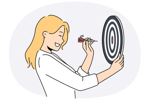 Determined woman throws darts at target for concept of business success and achieving set goals. Goal oriented businesswoman with darts board smiling setting and achieving ambitious goals