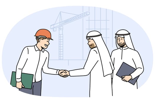 Handshake of arab businessmen and builder from architectural bureau standing near tower crane. Manager of international construction company makes important business deal with arab investors