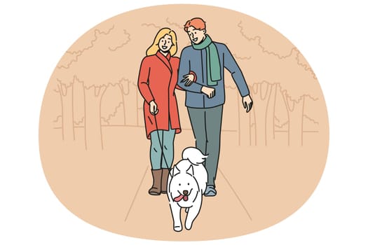 Man and woman are walking their dog together in park enjoying walk on autumn evening with warm weather. Happy couple with white dog on leash take care of pet in need of timely walk outdoors