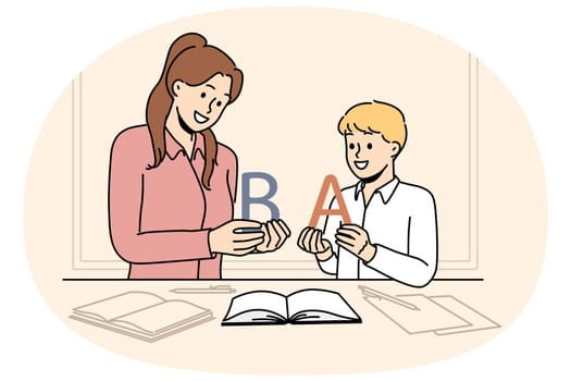 Back to school concept with boy learning alphabet along with elementary school teacher standing near table with books. Woman teaches child read or spell correctly, wanting give son quality education