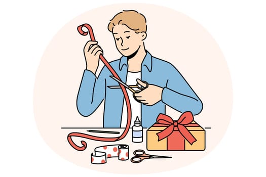 Man makes gift with own hands decorating box with red ribbon with festive paper. Romantic guy prepares beautiful DIY gift for valentine day and birthday and christmas for beloved girlfriend