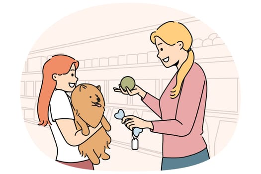 Girl with dog stands in ZOO shop near woman seller offering to buy toy bone for pet. Happy mom and little daughter choose rubber ball for their dog together after adopting puppy from shelter
