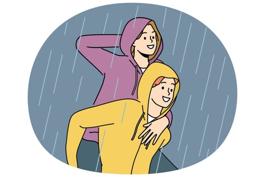 Happy couple walks in rain enjoying downpour after long drought and not wanting to go home. Man in waterproof hood rolls laughing girlfriend on back and enjoys autumn weather with rain