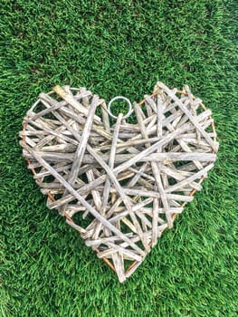 Wicker heart is on a green grass on a sunny day. Romantic background for a declaration of love, announcement of an engagement or other amorous event. Valentine. Event. San Valentine.