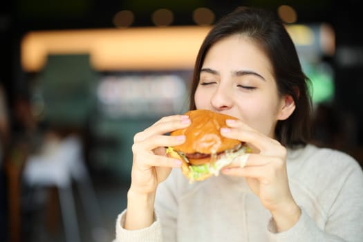 Happy woman eating burguer in a restaurant interior