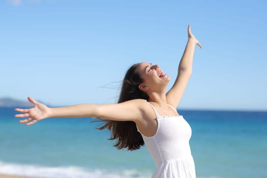 Joyful woman in white dress outstretching arms celebrating on the beach