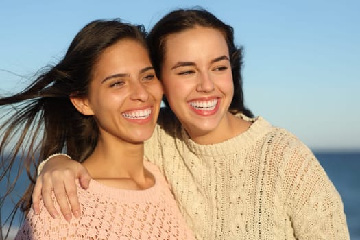 Two happy friends smiling looking away on the beach