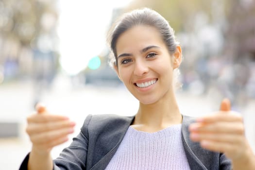 Front view portrait of a happy young executive saying follow me gesturing with hands in the street