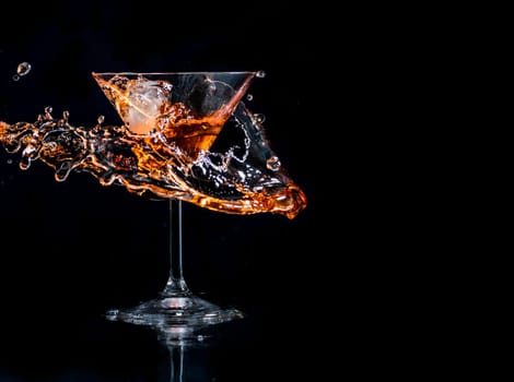 Cocktail splash in martini glass over black background with copyspace. Alcohol drink menu design. Cocktail happy hour and nightlife party concept.