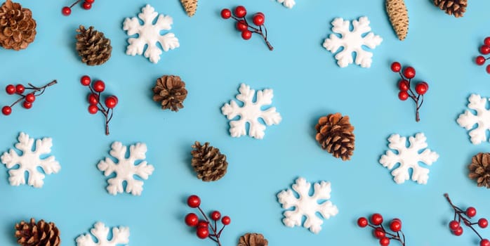 Minimal christmas, new year and winter holiday composition. Flat lay. Creative pattern banner with snow flakes, pine cone and red berries on pastel blue background. Christmas and wintertime concept.