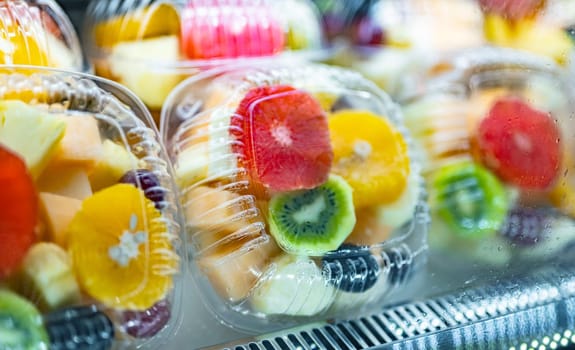 Plastic boxes with fresh fruits displayed in a commercial refrigerator. Fruit salad