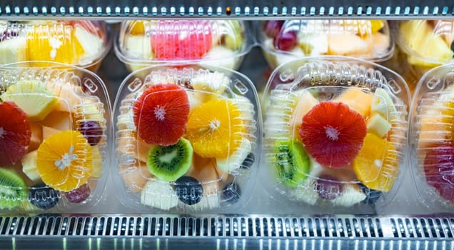 Plastic boxes with fresh fruits displayed in a commercial refrigerator. Fruit salad