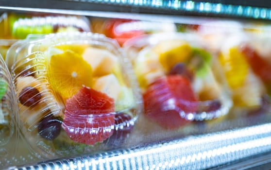 Plastic boxes with fresh fruits displayed in a commercial refrigerator. Fruit salad