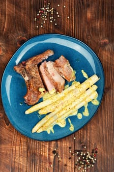 Sliced roasted meat steak with boiled white asparagus on rustic wooden table.