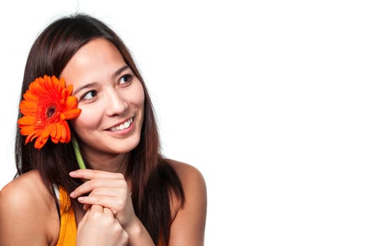 Side head and shoulders portrait of a young Asian woman looking to the side with a gerbera flower next to her face.