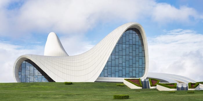 The iconic Heydar Aliyev Centre in Baku, Azerbaijan, showcases modern architecture with its fluid, wave-like design against a clear sky. Building designed by architect Zaha Hadid