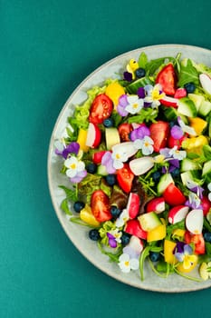 Colorful dietetics salad with vegetable and edible flowers. Top view.