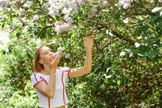 Adult redhead woman in tennis outfit sniffing lilac bush