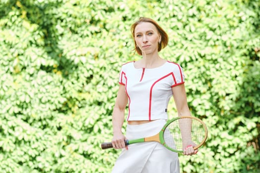 Adult redhead woman in tennis outfit posing with tennis racket
