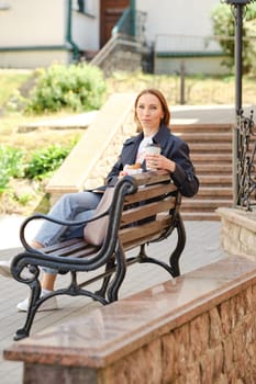 Red-haired middle aged woman sitting on bench holding coffee and croissant having fun