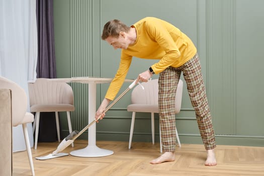Middle aged man doing housework, mopping floors in his living room