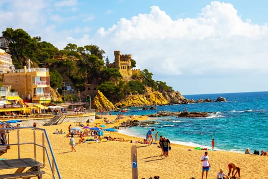Lloret de Mar, Catalonia, Spain, 02 October 2019. Tourists on the beach of Lloret de Mar below the Castell de Plaja, a castle-like house from the 1940s. Costa Brava.