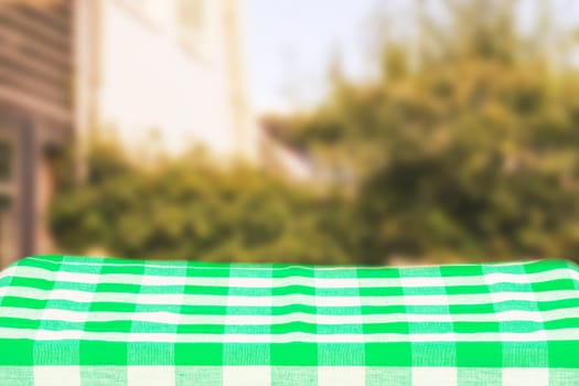 Empty table product. Empty colorful checkered tablecloth over abstract blurred natural green background texture with space for food and product display montage.