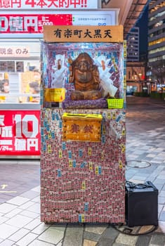 tokyo, japan - nov 29 2023: Donation box dedicated to one of the Seven Lucky Gods Daikokuten covered by votive slips named senjafuda in front of the Japan National Lottery shop of Yurakucho Station.