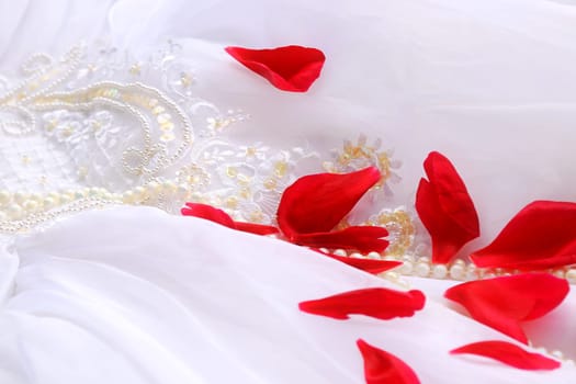 Close-up of a wedding dress with pearls and red rose petals