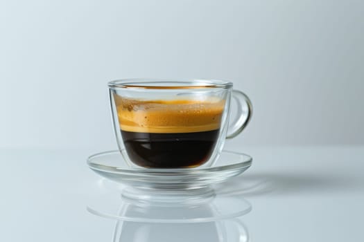 A cup of coffee with a glass saucer sits on a table. The coffee is dark and frothy, with a rich aroma. The cup is almost empty, with only a small amount of coffee left in it