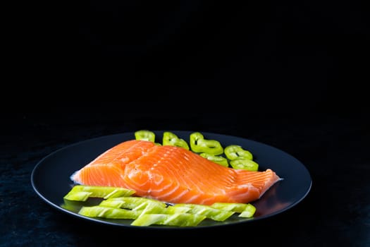 Salted fish salmon with pepper and onions on black plate. Top view. Free space for your text.