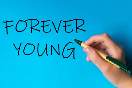 Children hand with pen write on a blue white background. Writing hand. Word Forever young