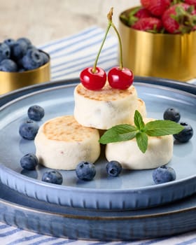Round small fried cheesecakes on a blue plate with berries. Healthy breakfast, close up