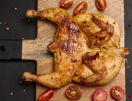 Whole fried chicken with spices on a wooden board on a black table, top view