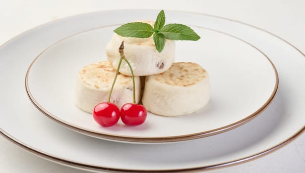 Round small fried cheesecakes on a plate with blueberries. Background white