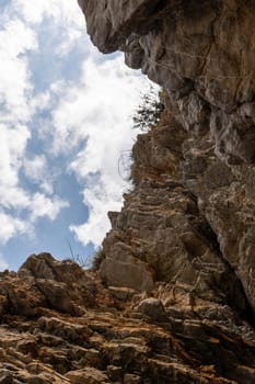 View of a rocky cliff against a blue sky with scattered clouds. Vegetation is visible on top of the cliff. Copy space.