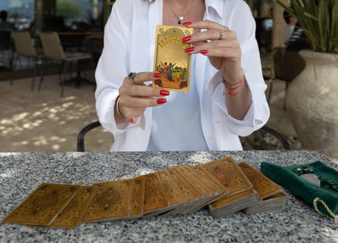Montenegro, Budva, May 6, 2024.A woman in a white blouse with red nails holds the Ten of Cups Tarot card while other Tarot cards are laid out on a table.Rider-Waite Tarot