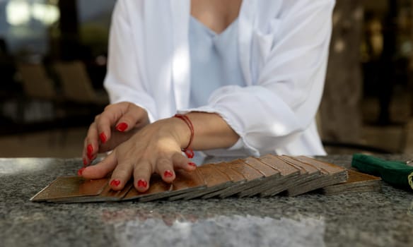 Close-up of a woman's hands spreading tarot cards on a granite table in a cafe, focusing on her hands and red nails. fortune telling.lifestyle or spirituality content