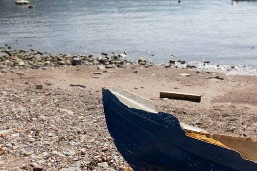 Broken blue boat on a pebble beach with the sea in the background. the aftermath of a storm on a sunny day. Copy space.Suitable for nature or abstract content