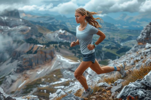 A woman in athletic attire runs with purpose along a rocky mountain trail, her determined gaze fixed on the horizon. The scenic backdrop of towering peaks and cloudy skies paints a picturesque landscape, capturing the essence of a challenging yet rewarding outdoor adventure.