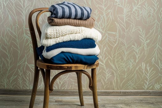 Stack of folded knitted warm clothes on a chair. Change of wardrobe for the winter season.