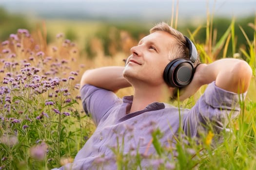 Handsome Caucasian Man Sitting in Flower Field Listening to Music in Headphones.