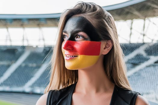 German fan waiting for match in sports stadium with German flag painted on her face.